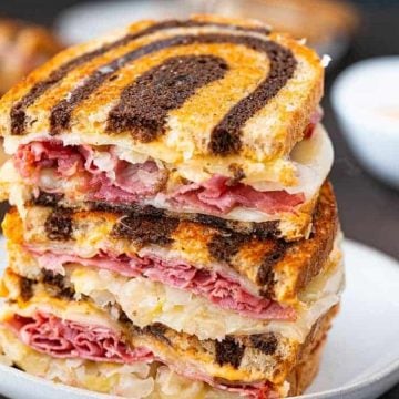 Three stacked Reuben sandwiches on marbled rye bread, filled with corned beef, sauerkraut, and cheese.