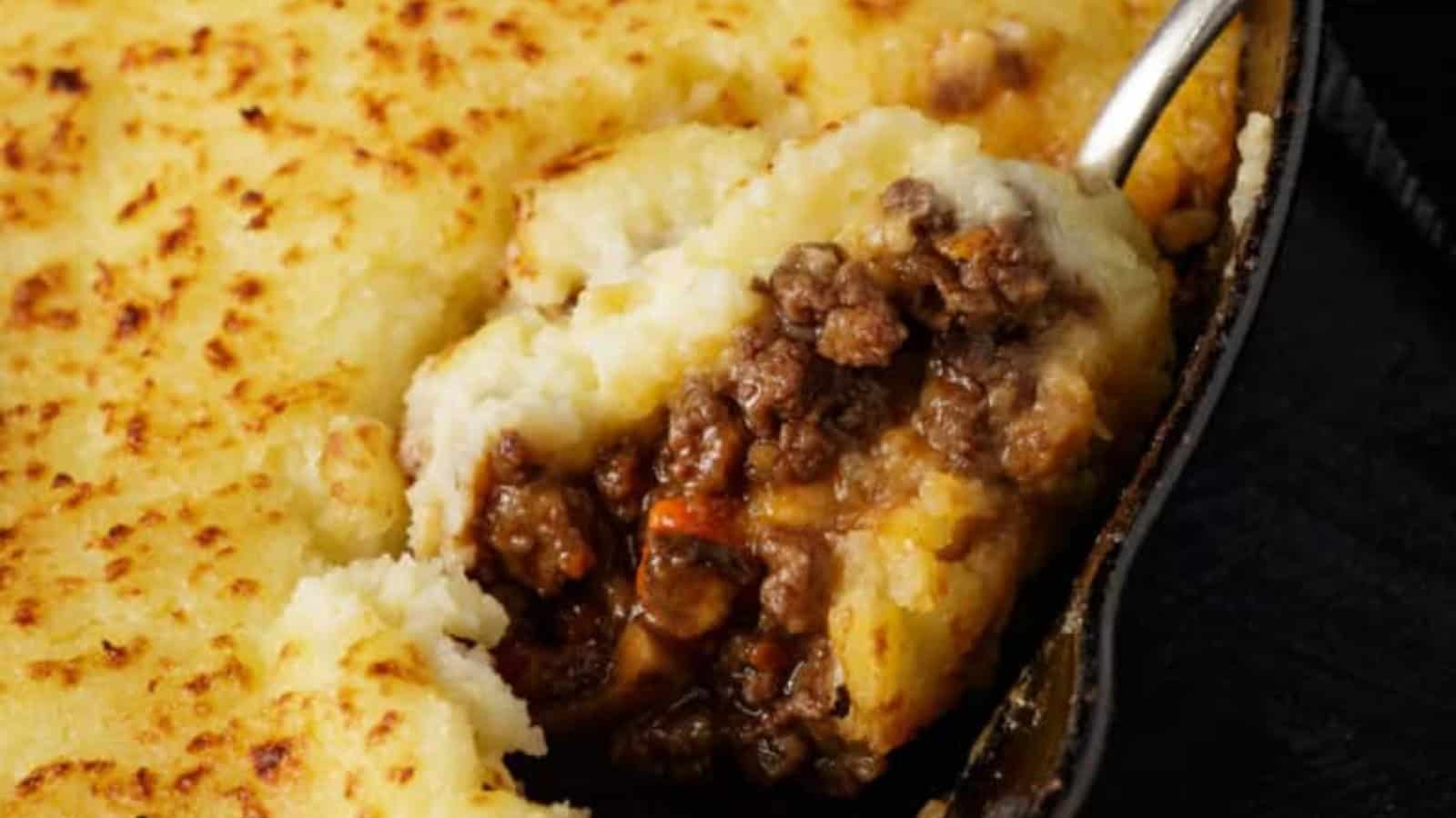 A spoon scoops out a serving of shepherd's pie topped with golden mashed potatoes.