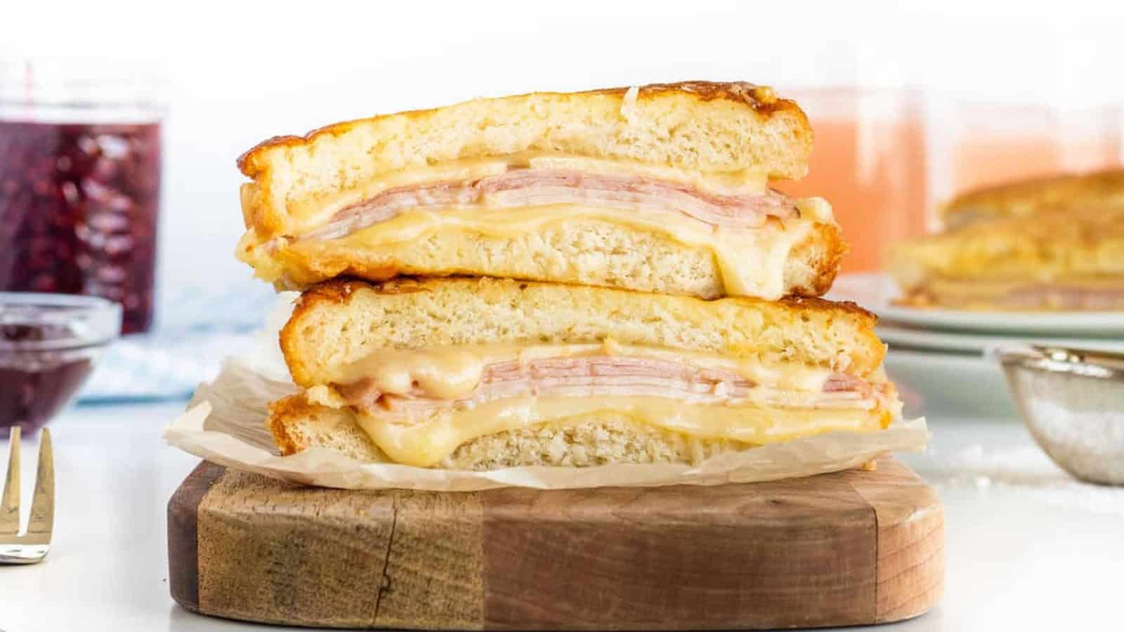 Stacked ham and cheese sandwiches on a wooden board, with melted cheese oozing out.