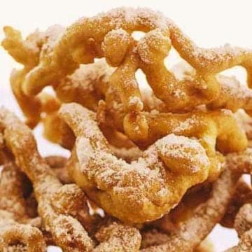 Golden, sugar-dusted funnel cakes stacked against a light background.