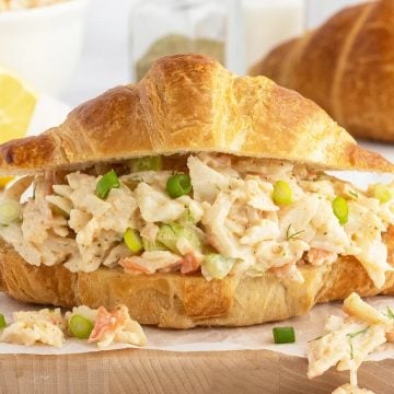 A croissant sandwich filled with creamy chicken salad, garnished with green onions, on a wooden board.