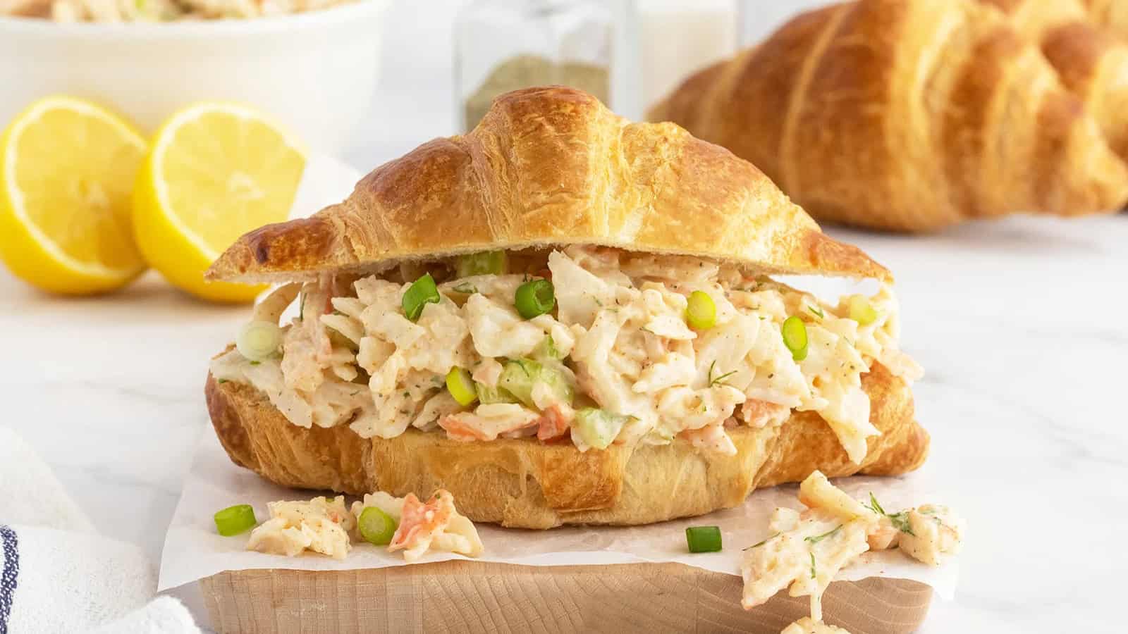 A croissant sandwich filled with creamy chicken salad, garnished with green onions, on a wooden board.