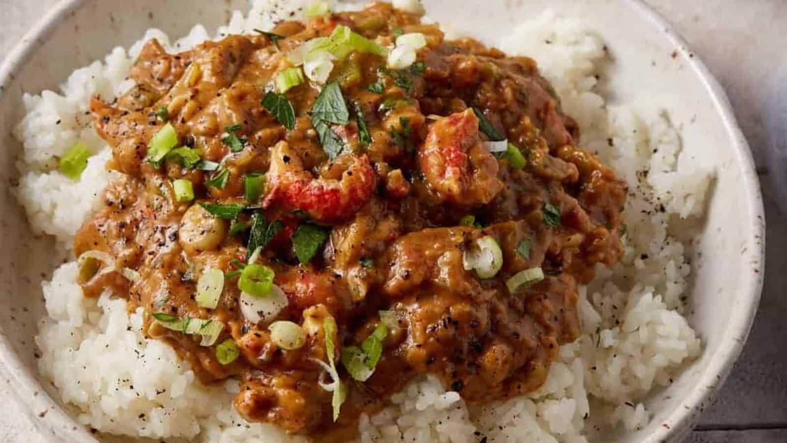 A bowl of white rice topped with a creamy stew, garnished with chopped green onions and herbs.