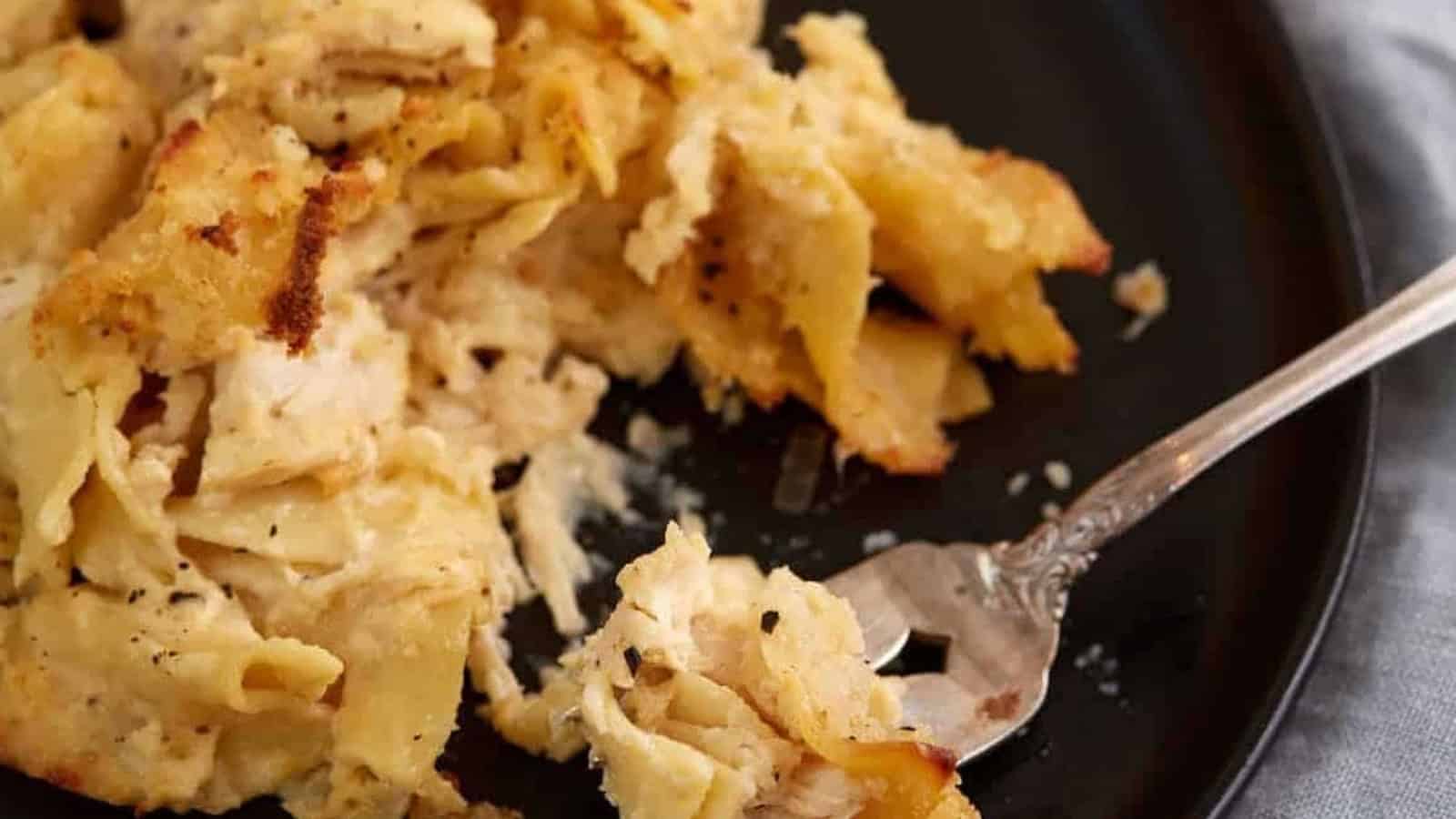 A close-up of a serving of chicken casserole on a black plate with a fork.