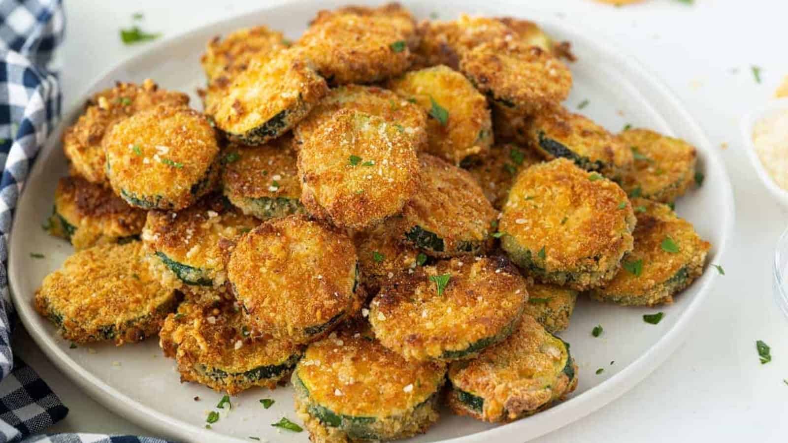A plate of golden-brown breaded zucchini chips garnished with chopped parsley.