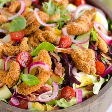 Salad with breaded chicken, cherry tomatoes, red onions, avocado, greens, and sliced boiled eggs in a bowl.