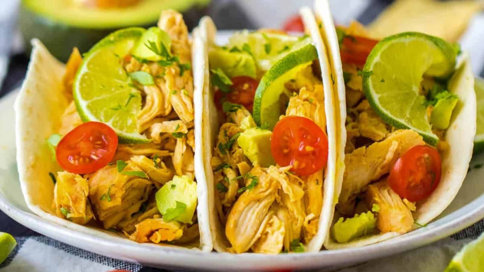 Three slow cooker tacos with chicken, lime, avocado and tomatoes.