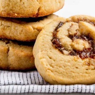 Four thick cookies, one with a swirled filling, rest on a striped cloth on a white surface.