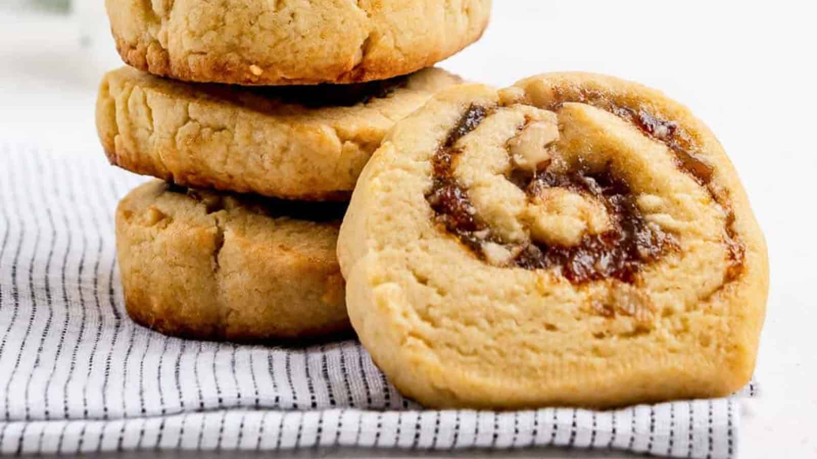 Four thick cookies, one with a swirled filling, rest on a striped cloth on a white surface.