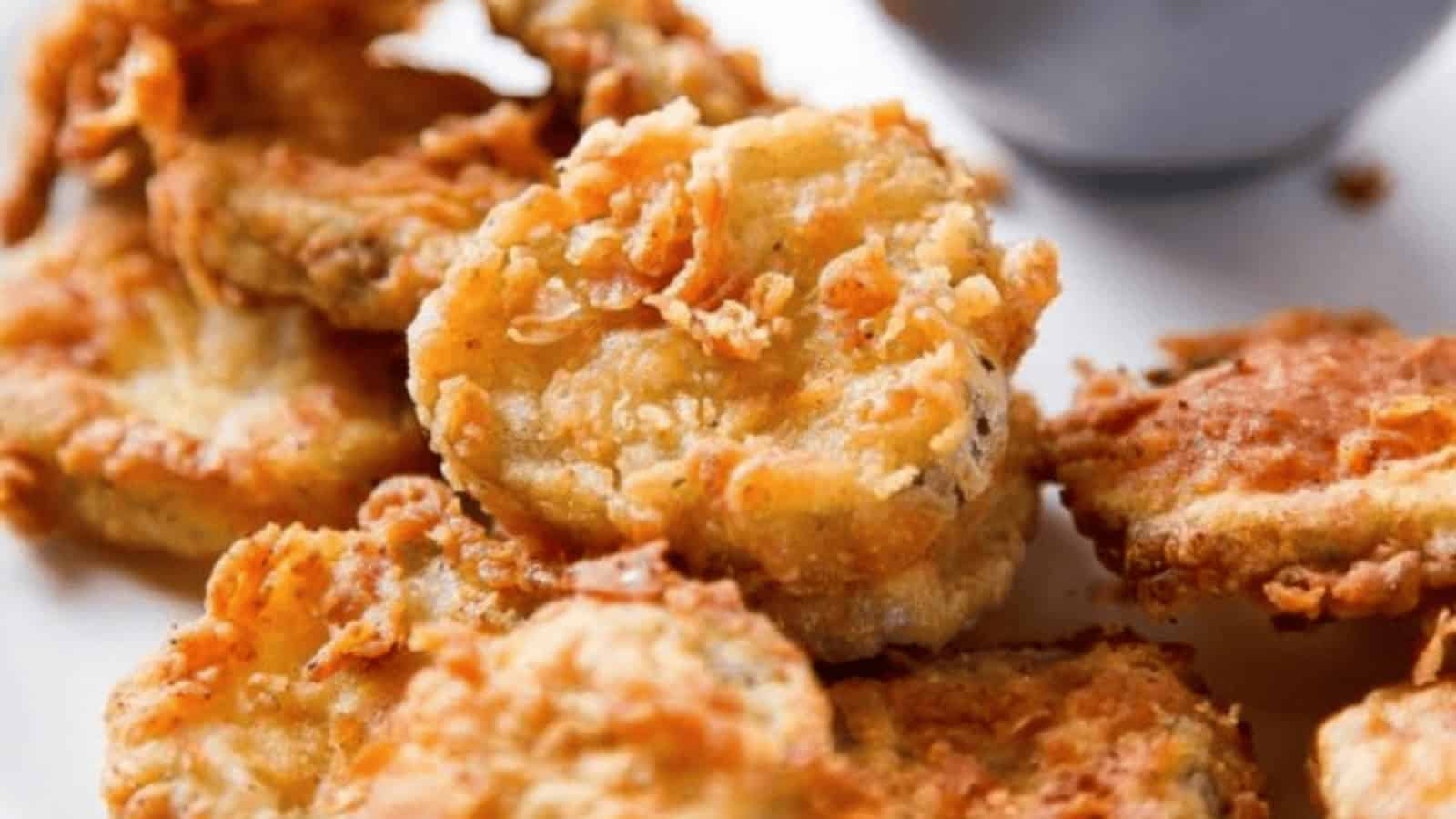 Close-up of crispy, golden fried pickles on a white plate with a dipping sauce in the background.