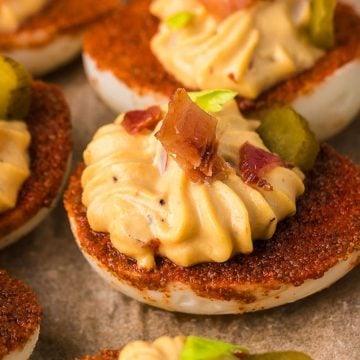 Deviled eggs topped with bacon, seasoning, and sliced pickles arranged closely on a tray.