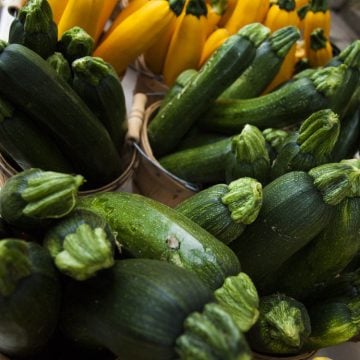 Baskets filled with green and yellow zucchini are displayed on a market stand.