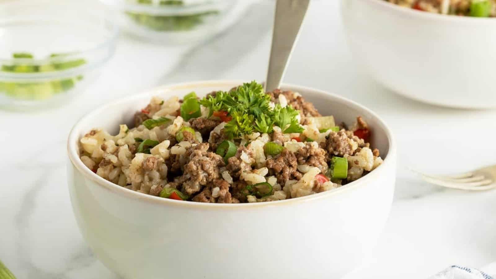 A bowl of rice with ground beef, green herbs, and a fork, garnished with parsley.
