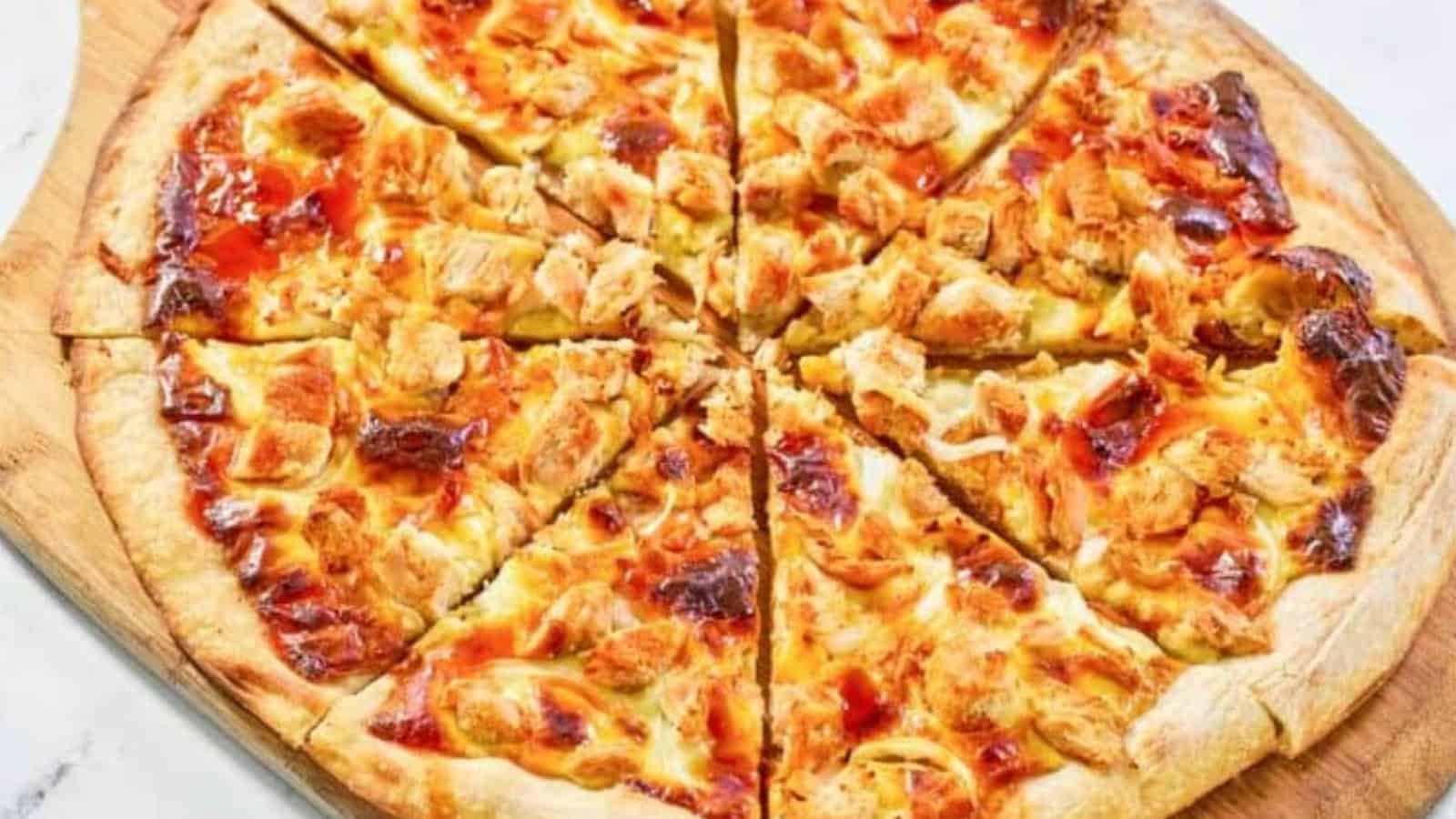 A baked pizza with barbecue sauce and chunks of chicken, sliced into eight pieces on a wooden board.