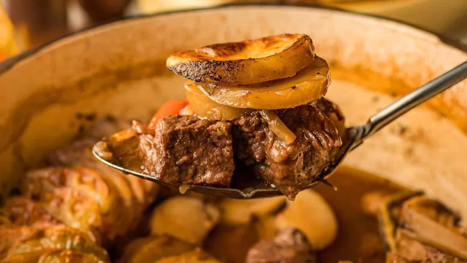A spoon holds beef stew with potato slices and vegetables over a pot filled with more stew.