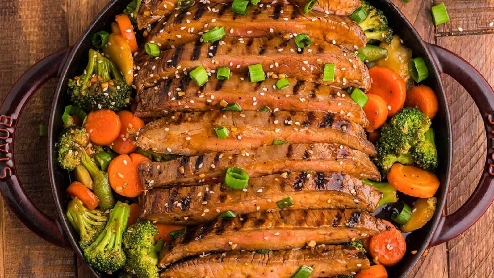 Sliced grilled steak topped with sesame seeds and green onions, served with broccoli and carrots in a skillet.