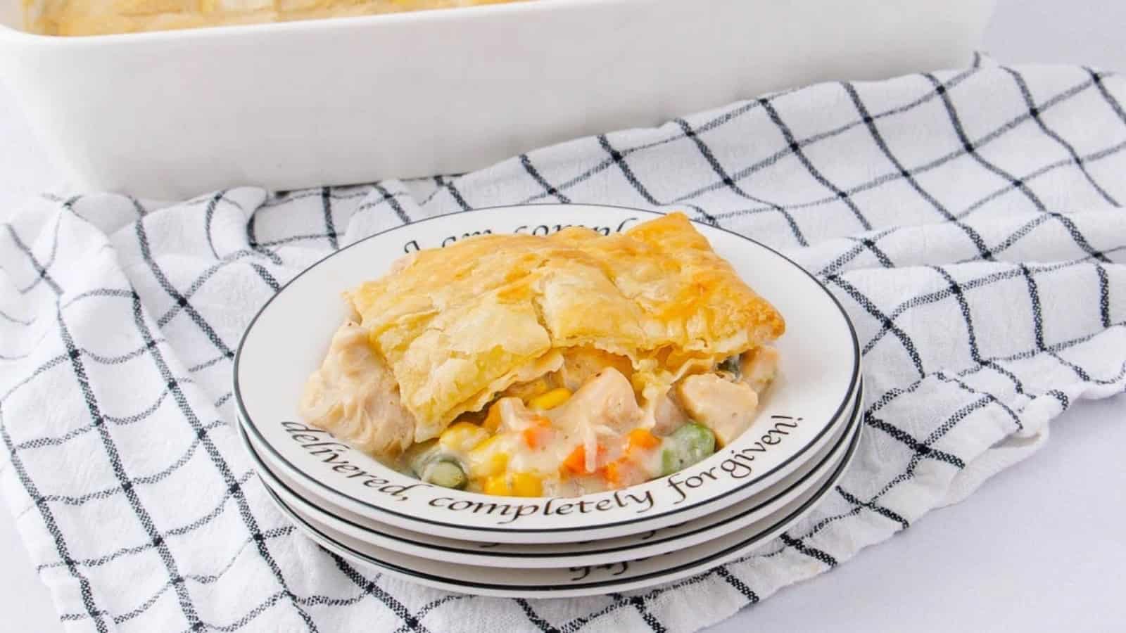A slice of chicken pot pie on a stack of plates, set on a checkered kitchen towel.