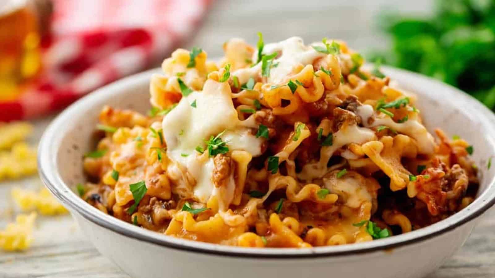 A bowl of rotini pasta with meat sauce and melted cheese, topped with fresh parsley.