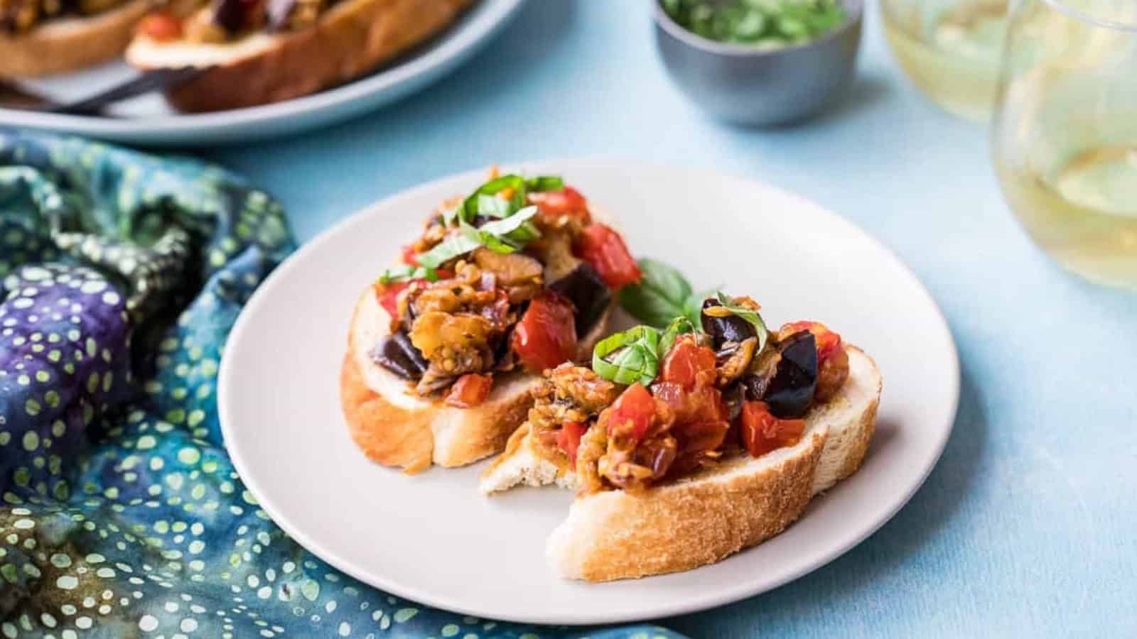 Two slices of bread topped with a tomato and vegetable mixture, garnished with basil on a white plate.