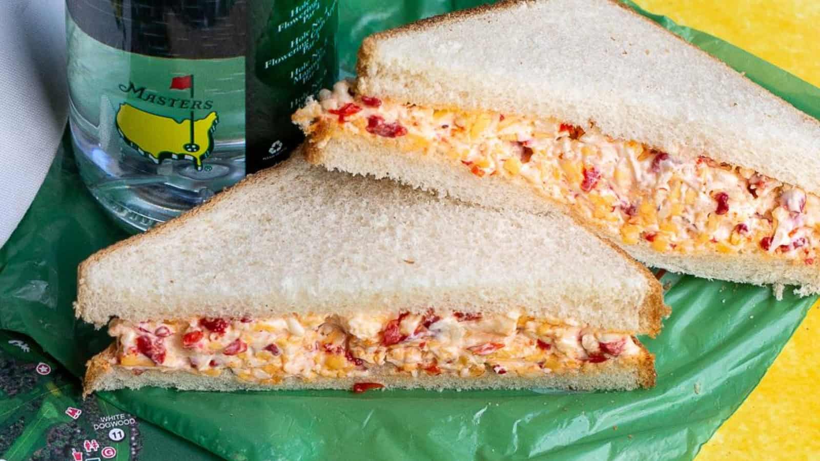 Pimento cheese sandwich on white bread, sliced in half, beside bottled water with Masters logo.