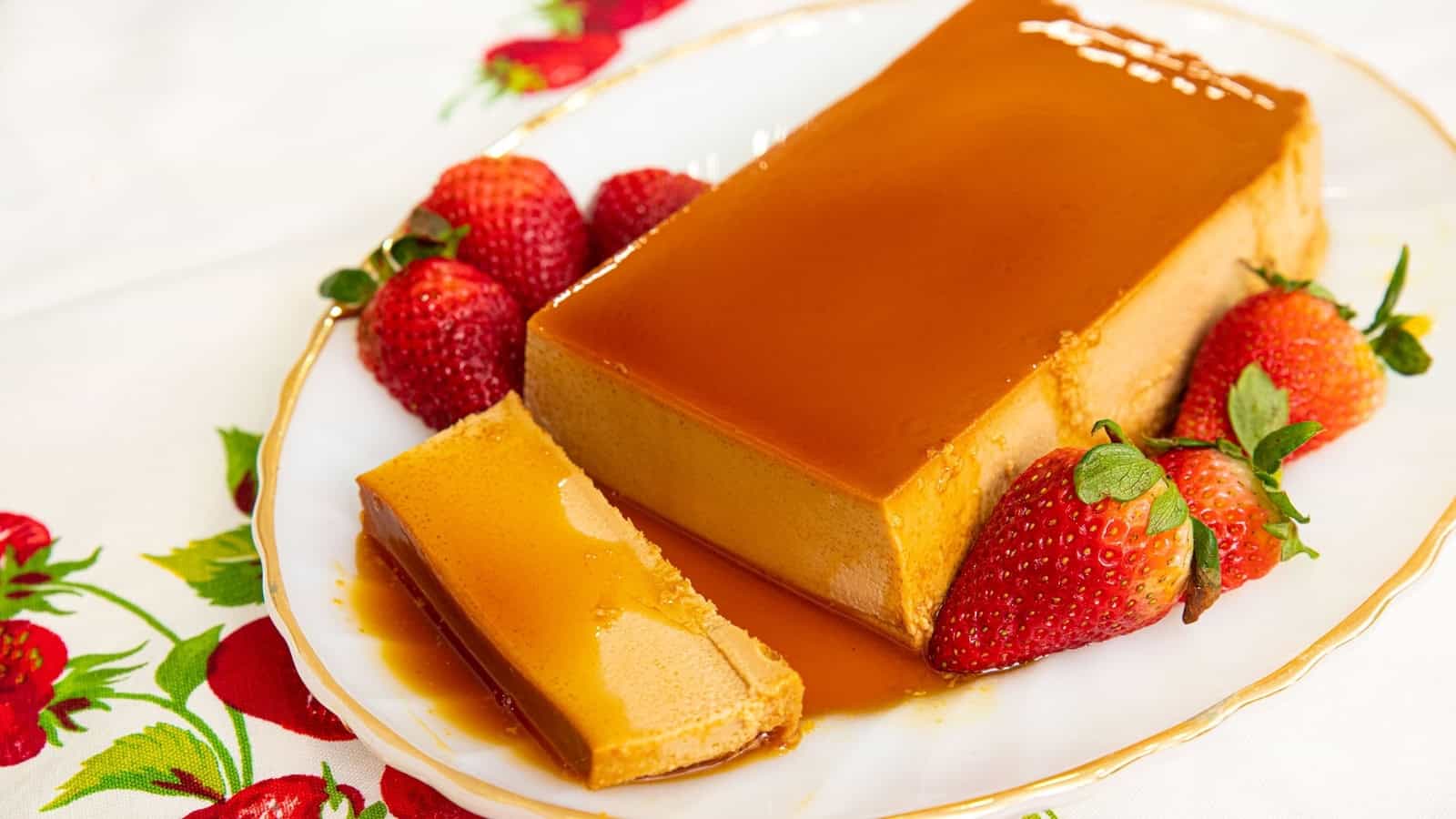Rectangular caramel flan on a plate with strawberries, with one slice cut and served.