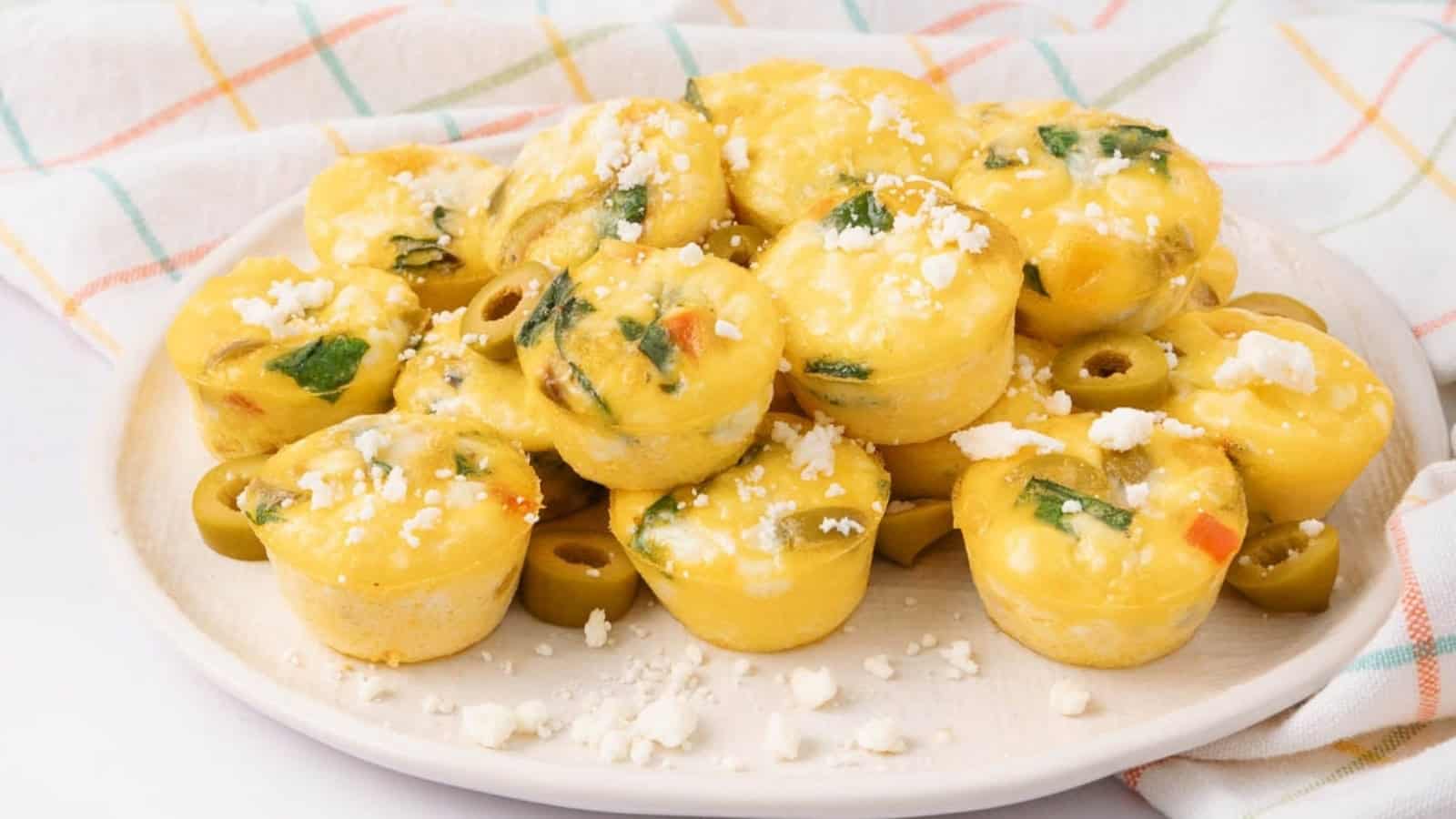 Mini egg muffins with spinach, veggies, and cheese on a white plate, on a plaid napkin background.