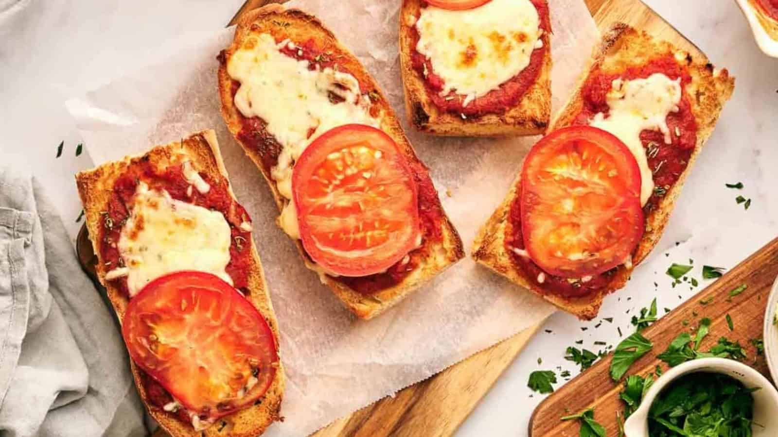 Four slices of French bread pizza with tomatoes and cheese on a cutting board.