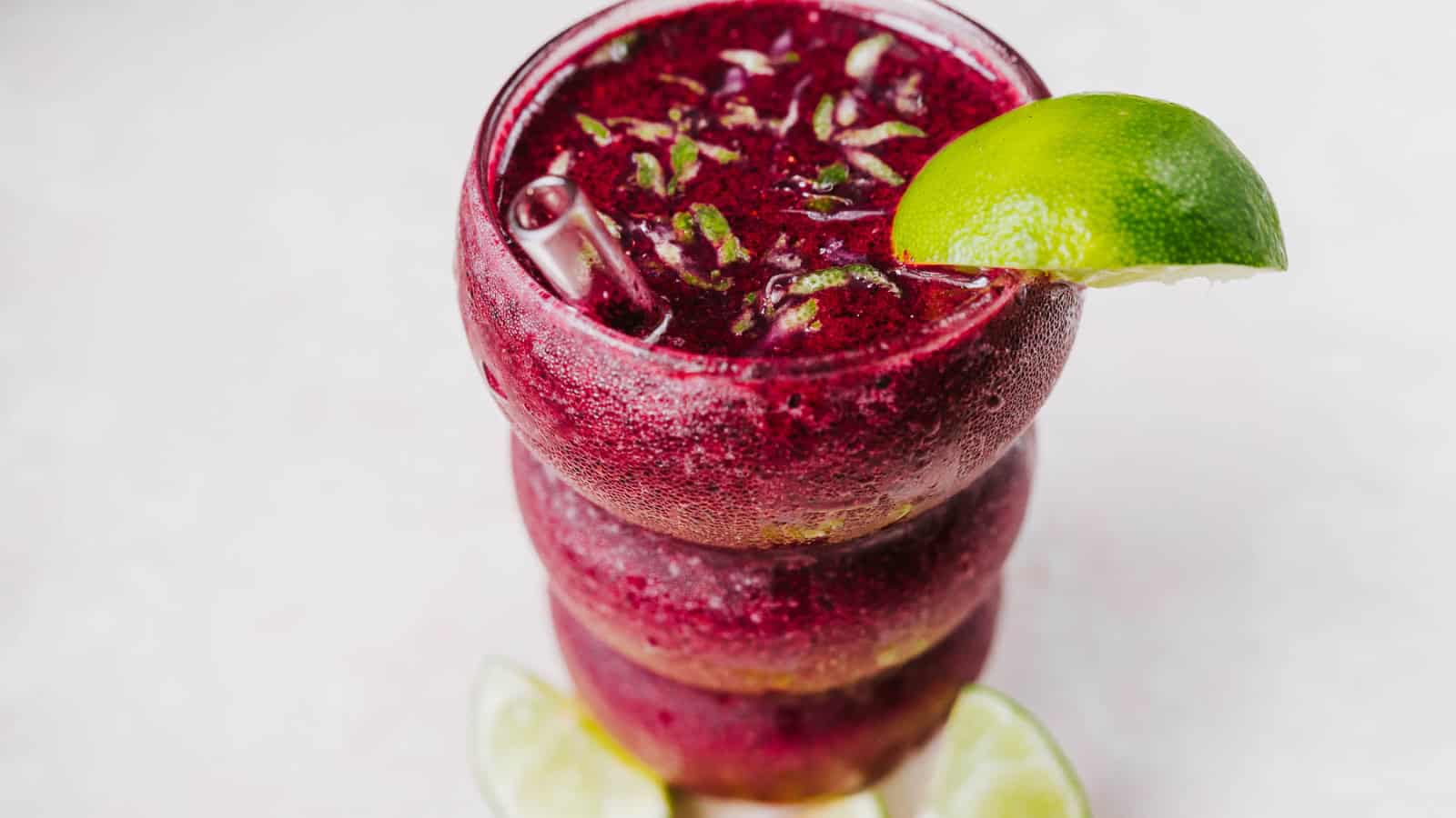 A purple frozen drink in a glass, garnished with a lime wedge and slices, viewed from above.