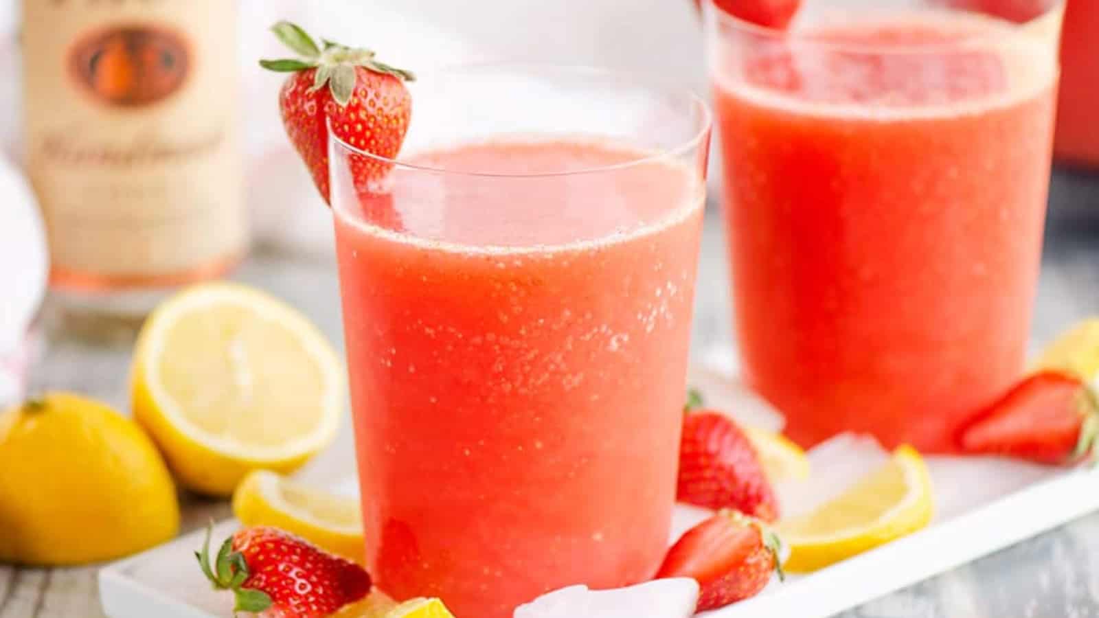 Two glasses of strawberry lemonade with ice, lemon slices, and strawberries on a tray.