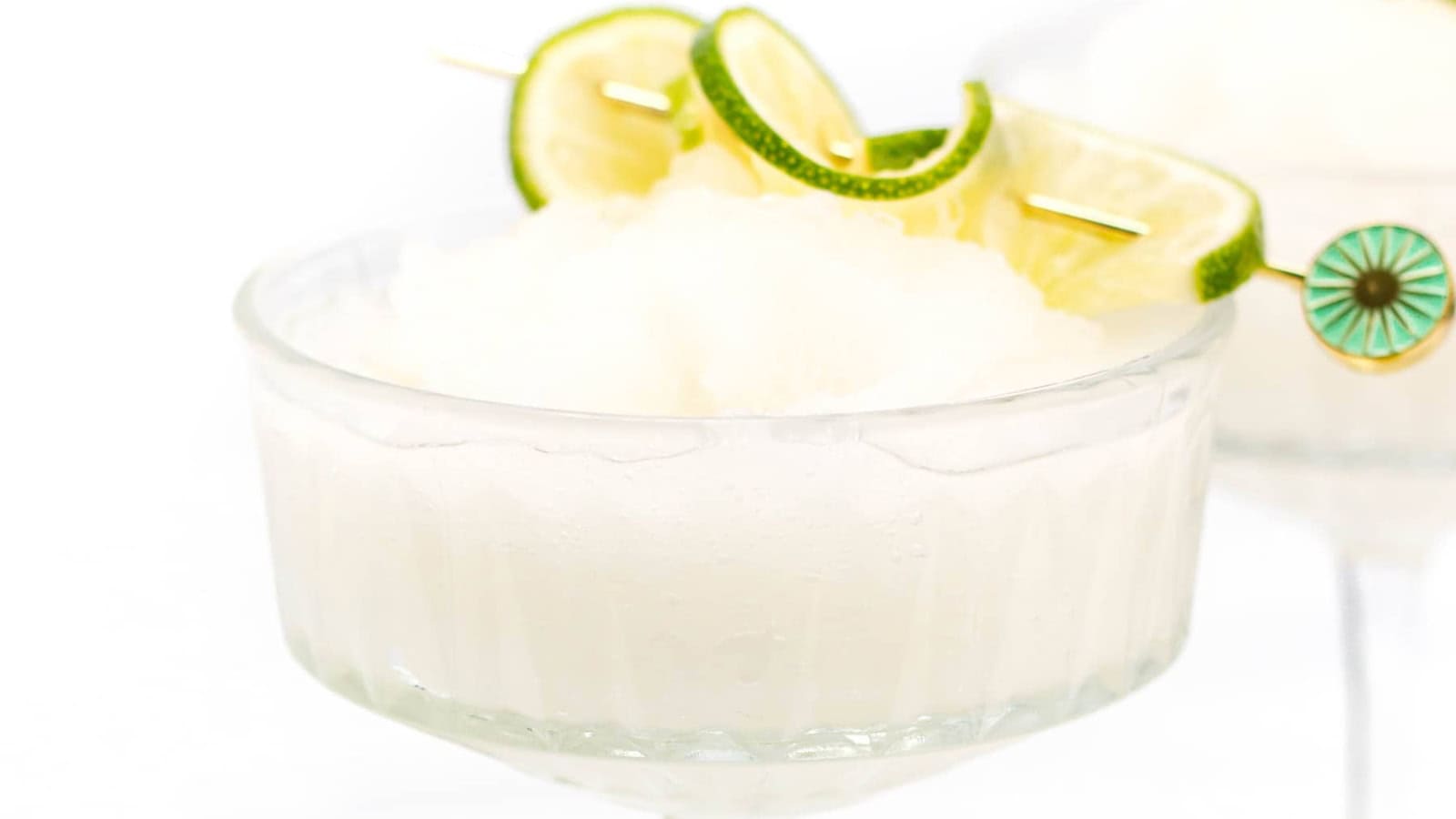 Frozen margarita in a glass, garnished with lime slices on a cocktail pick, against a white background.