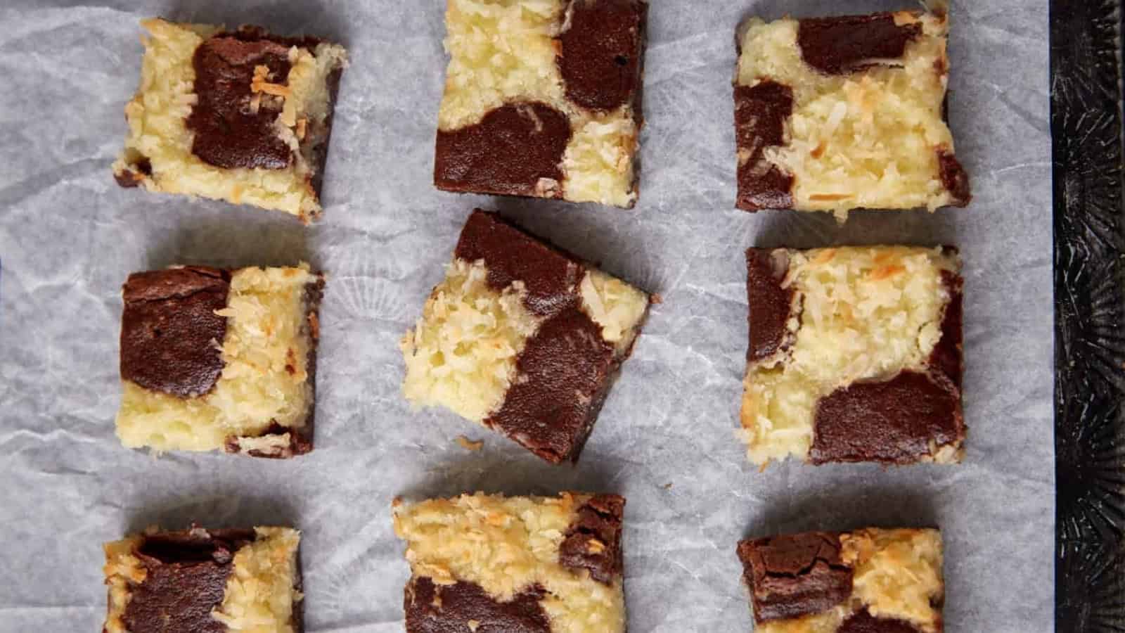 Nine coconut and chocolate marbled brownies on parchment paper, arranged in a three-by-three grid.