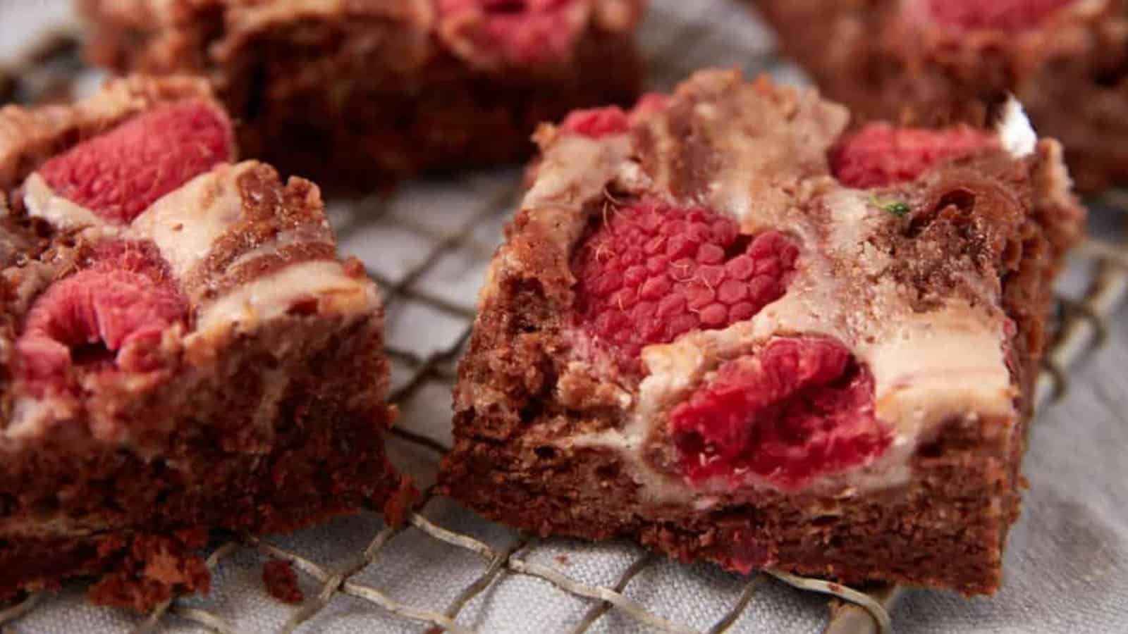 Close-up of chocolate raspberry brownies with a creamy swirl, resting on a cooling rack.