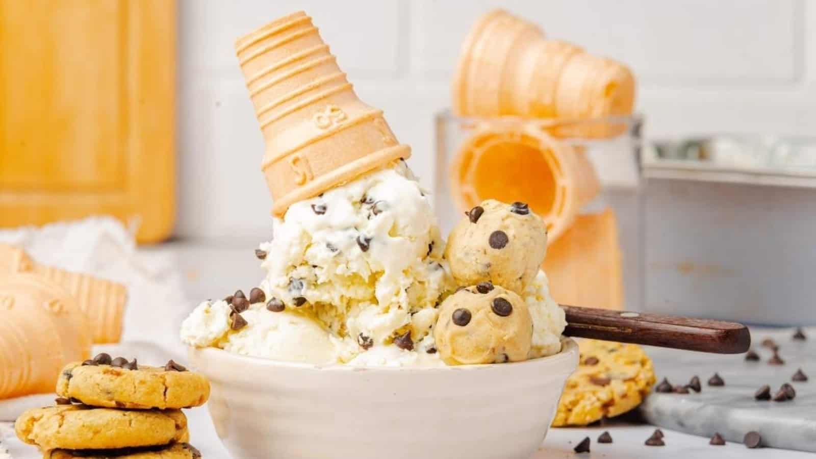 A bowl of ice cream with chocolate chips, cookie dough balls, and an upside-down cone on top.
