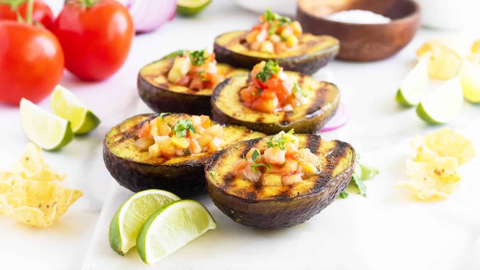 Grilled avocado halves filled with salsa, garnished with cilantro, and served with lime wedges and tortilla chips.