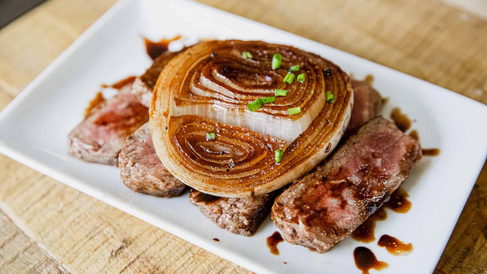 Grilled balsamic onion slices served over steak with balsamic sauce and chopped chives.