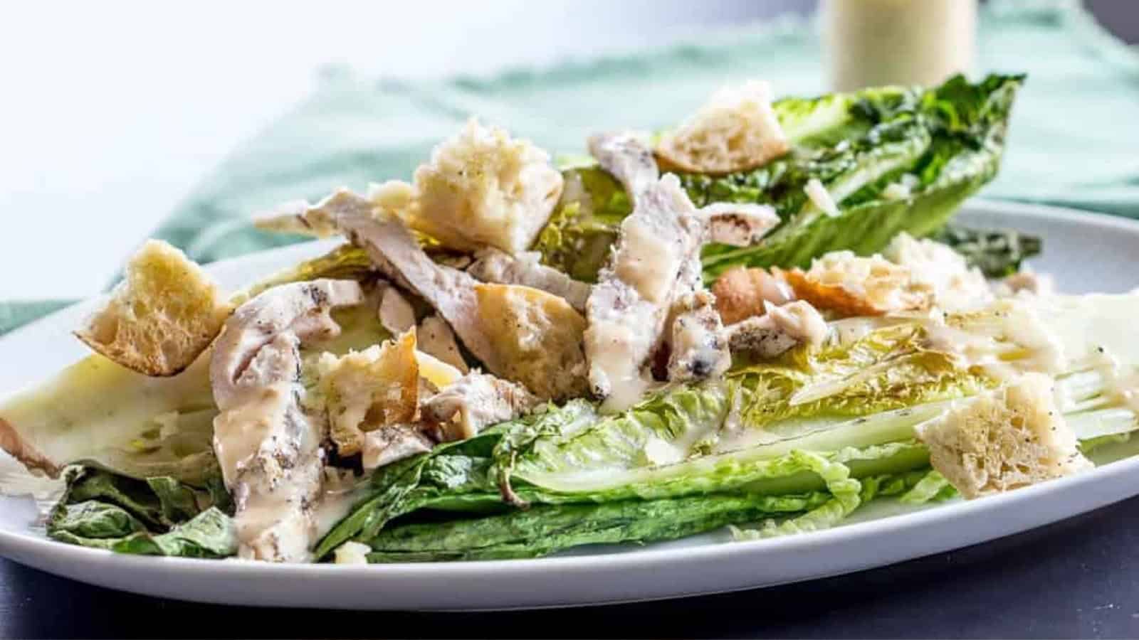 Grilled chicken Caesar salad with romaine lettuce, croutons, and creamy dressing on a white plate.