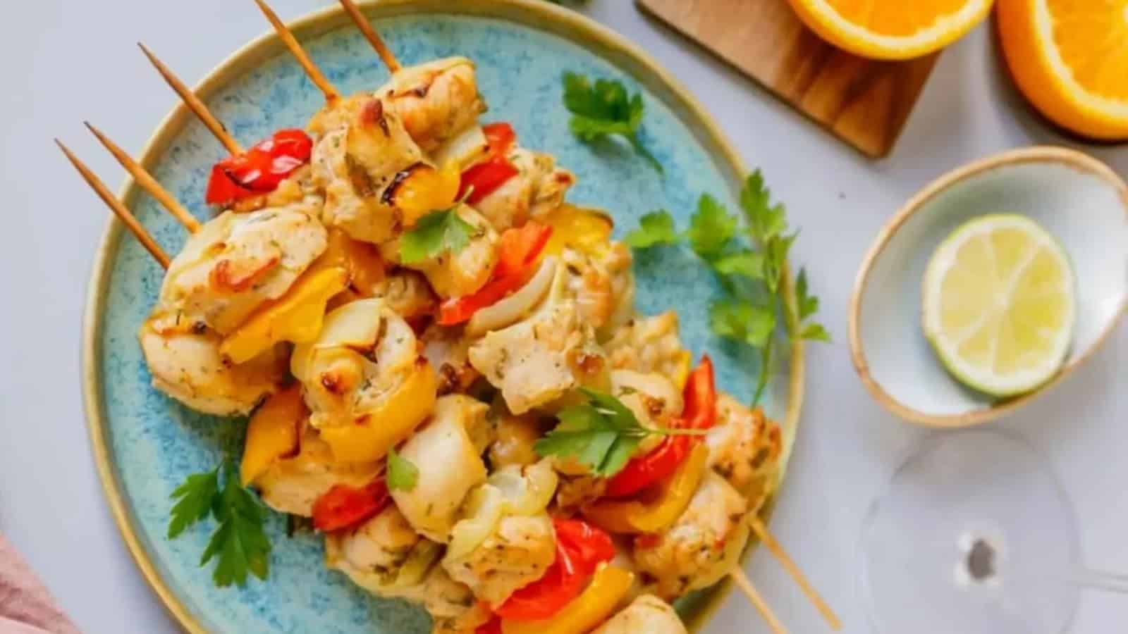 Chicken and vegetable skewers on a blue plate, garnished with parsley, with orange and lime slices nearby.