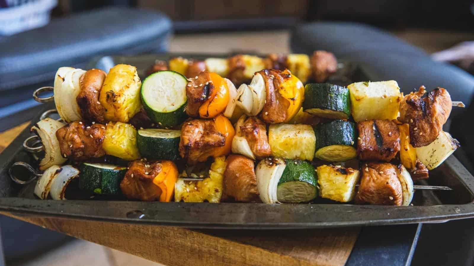 A tray of grilled skewers with chicken, zucchini, onions, pineapple, and bell peppers.