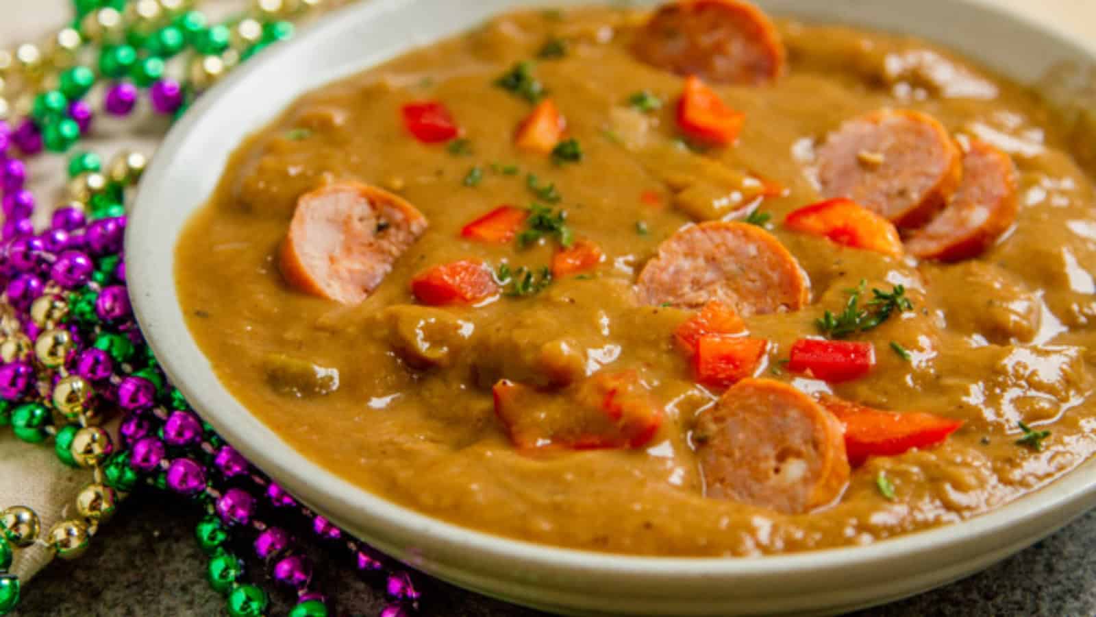 Bowl of gumbo with sliced sausage, red peppers, and parsley, next to colorful Mardi Gras beads.