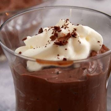 A glass cup of chocolate mousse topped with whipped cream and chocolate shavings.