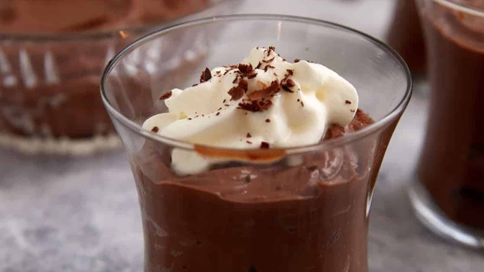 A glass cup of chocolate mousse topped with whipped cream and chocolate shavings.