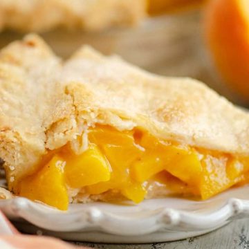 A slice of peach pie sits on a white plate, showing golden peach filling and a flaky crust.