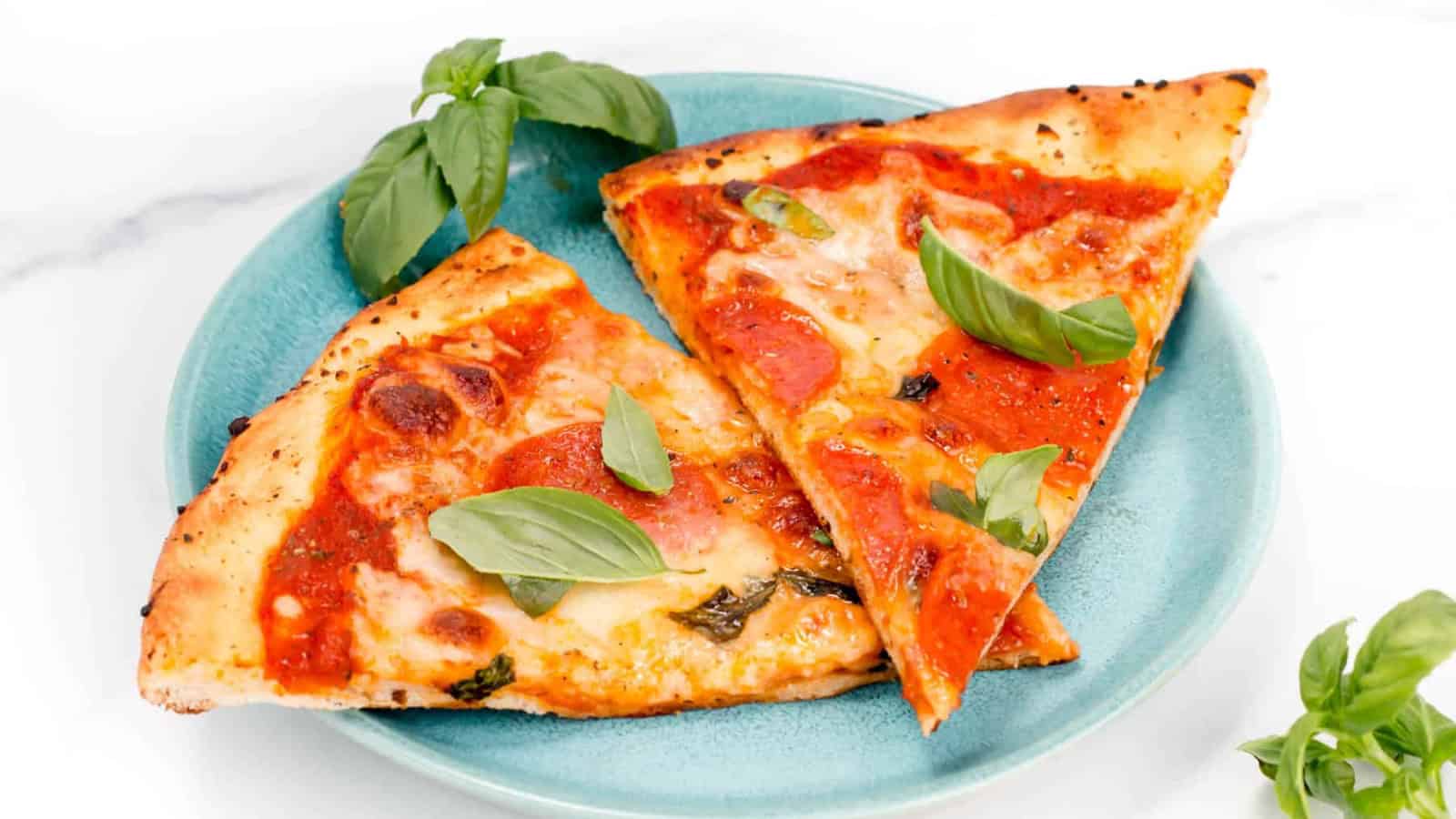 Two slices of Margherita pizza with fresh basil leaves on a blue plate, garnished with extra basil.