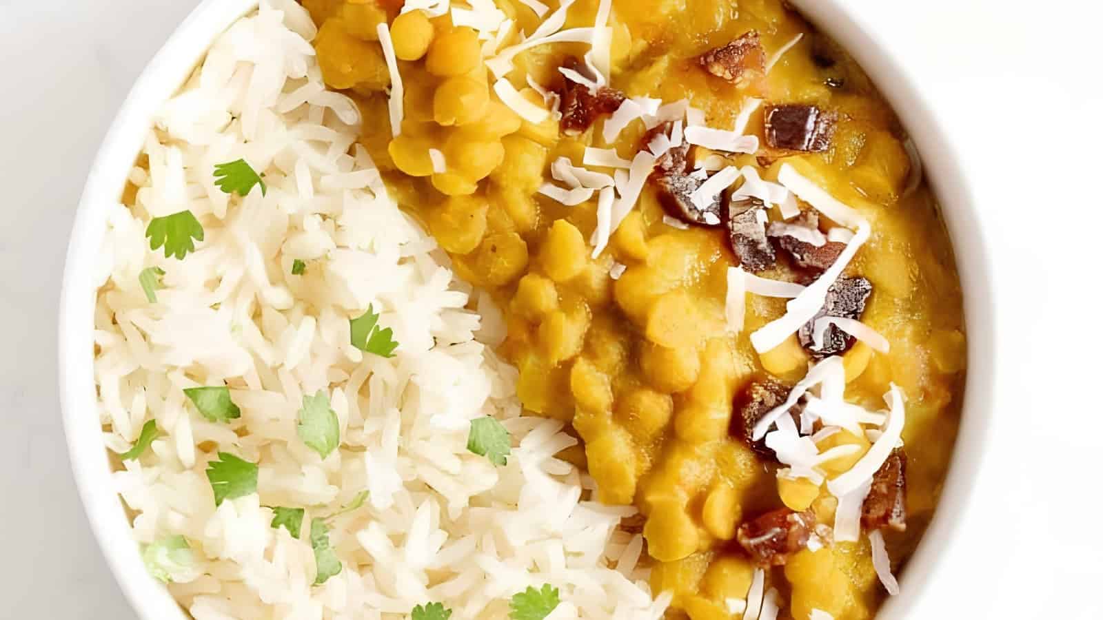 White rice with cilantro beside yellow lentil curry, topped with shredded coconut and small red garnish in a bowl.