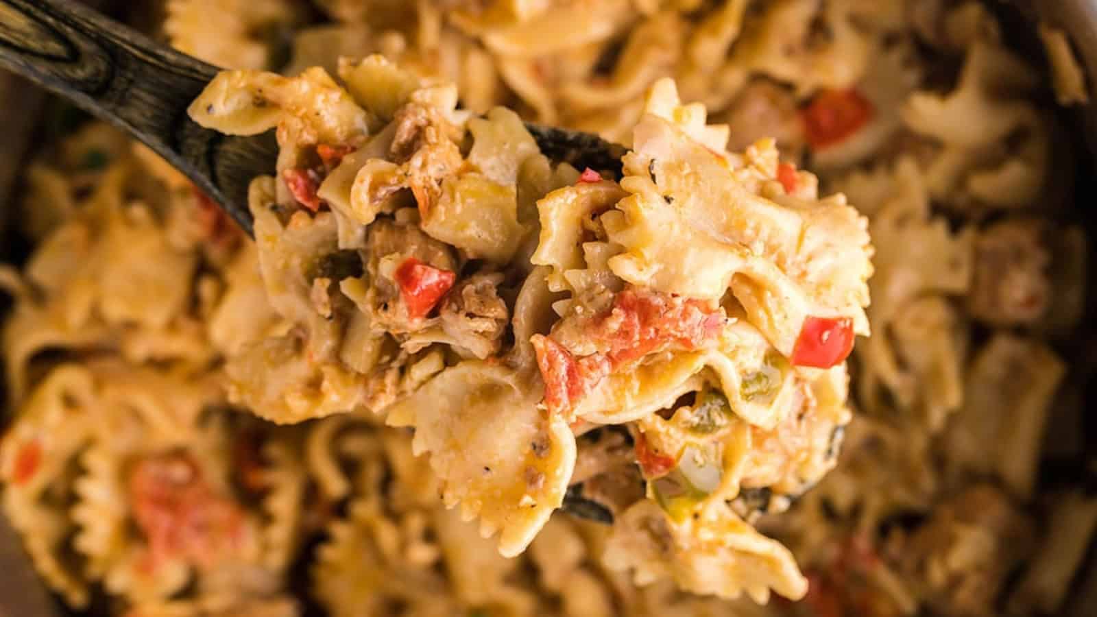 Spoonful of creamy bowtie pasta with diced tomatoes, bell peppers, and herbs.