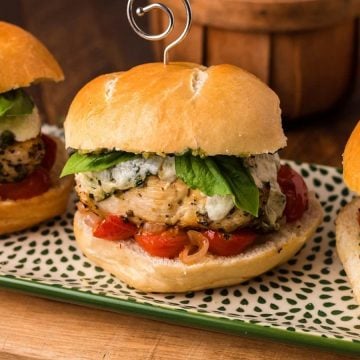 Three chicken burgers on a patterned plate, topped with cheese, fresh basil, and tomatoes.