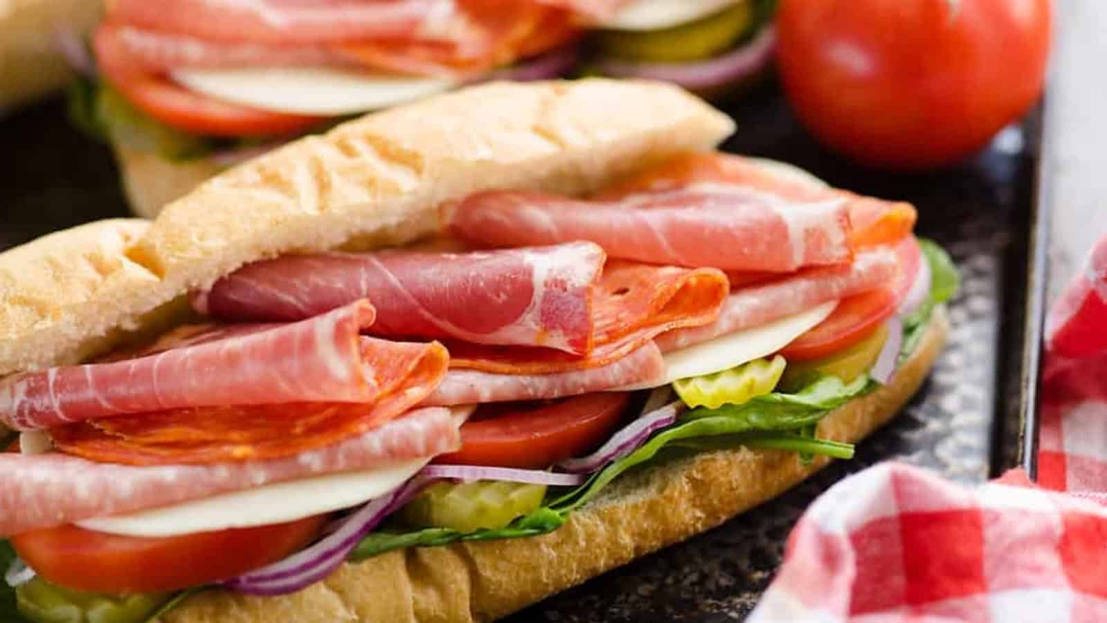 Italian sub sandwich with deli meats, cheese, tomato, lettuce, onion, and pickles on a baguette.