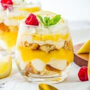 A delightful glass dessert, these Lemon Cheesecake Trifle Cups feature layers of cream, lemon curd, and cake, all topped with fresh raspberries, mint, and a bright lemon slice.