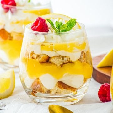 A delightful glass dessert, these Lemon Cheesecake Trifle Cups feature layers of cream, lemon curd, and cake, all topped with fresh raspberries, mint, and a bright lemon slice.