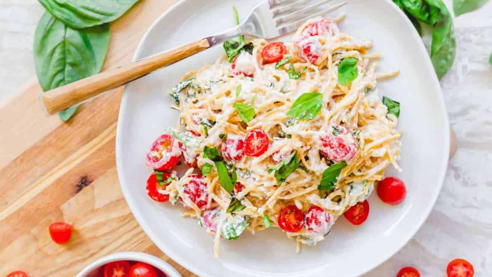 Plate of creamy pasta with cherry tomatoes, basil, and a fork on a white plate, overhead view.